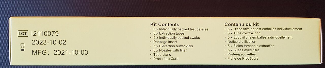 A COVID-19 rapid-antigen kit box shows a lot number, a 2023 expiry date, and bilingual lists of swabs, extraction tubes, buffers, and test devices.