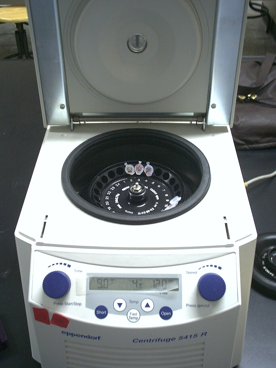 An open research microcentrifuge shows a rotor, several small tubes, and its control panel.