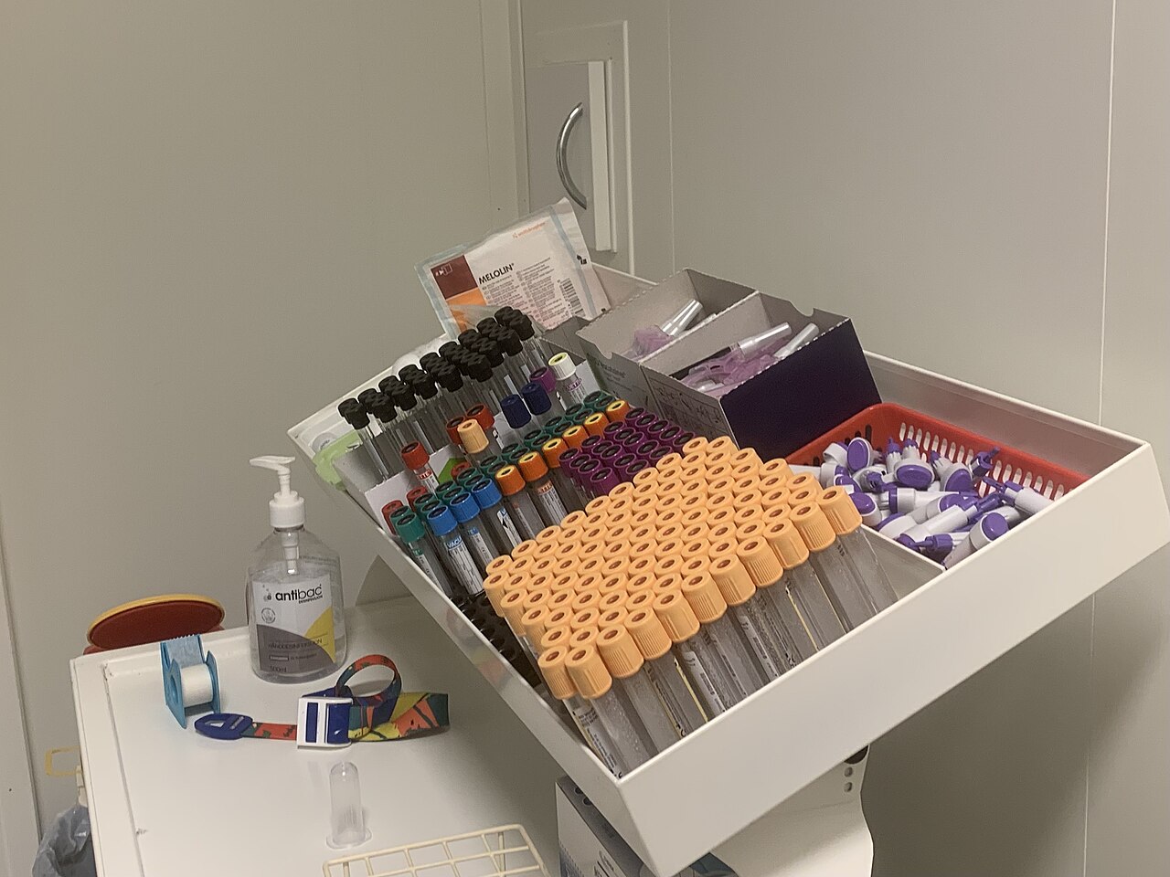 Blood collection tubes, holders, a tourniquet, gauze, and a hand-rub bottle arranged at a clinic work area.
