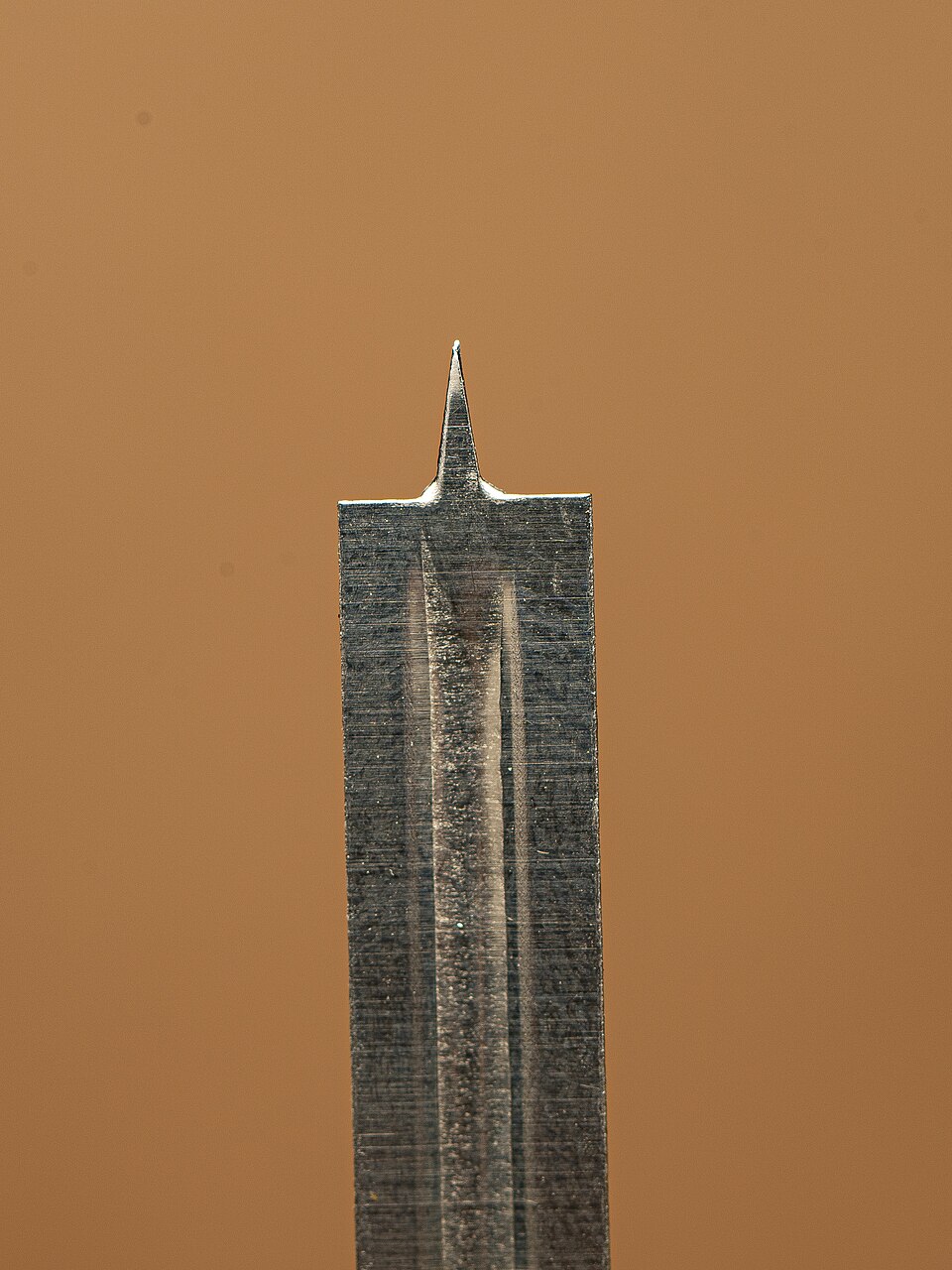A close-up photograph shows the pointed metal tip of an exposed lancet against a brown background.