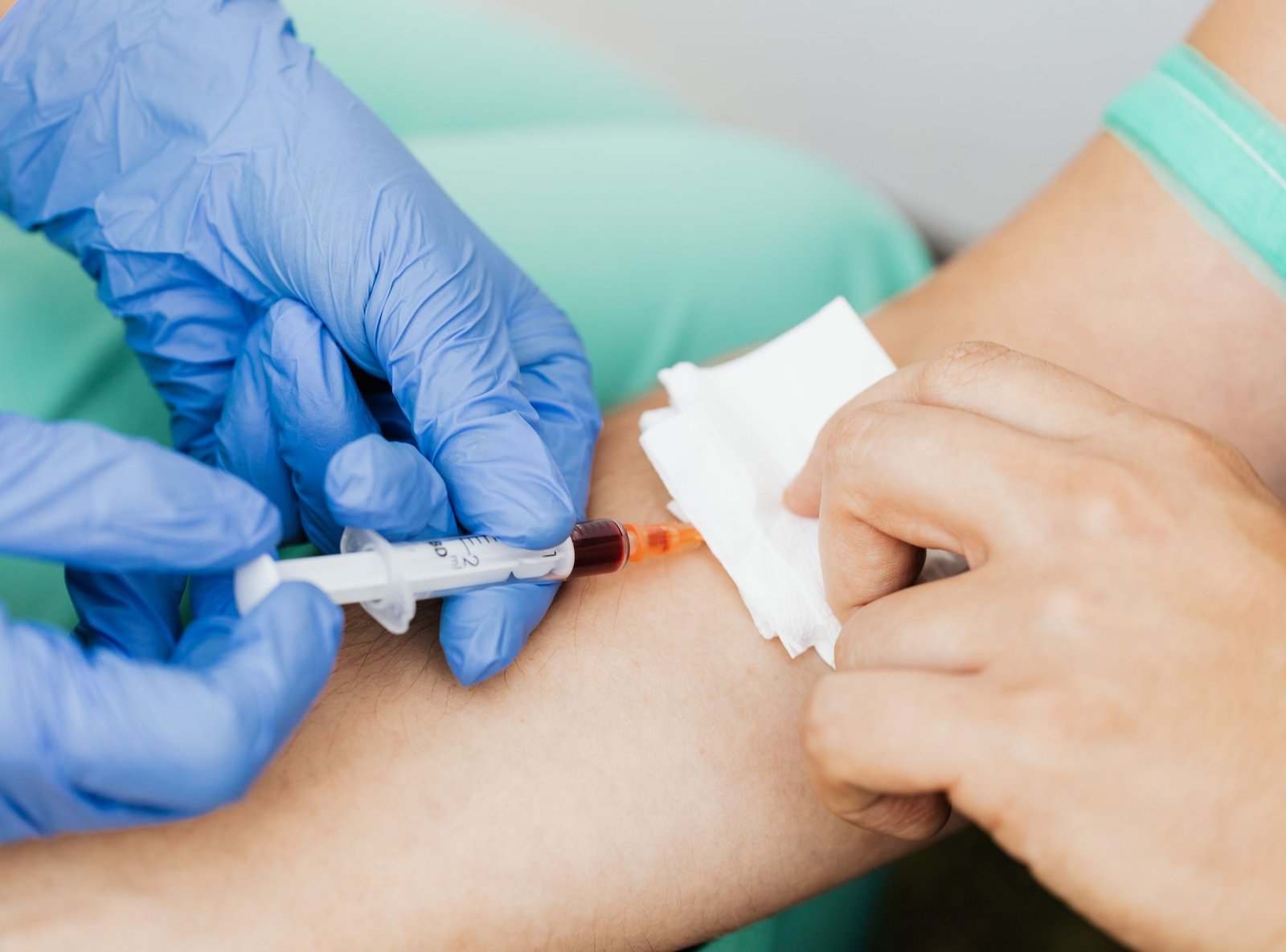 Gloved hand performing venipuncture with a syringe, blood visible in the barrel, tourniquet on the upper arm